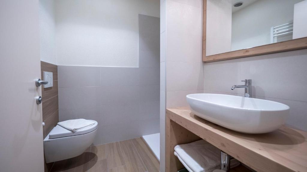 Mūsdienīgs vannas istabas interjers ar elegantu izlietni un minimālistisku dizainu, kas ietver dušas stūri un koka elementus. Ideāls risinājums komfortablai un stilīgai telpai.