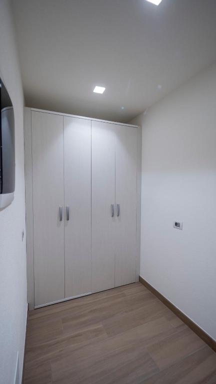 Mūsdienīgs guļamistabas skats ar baltām skapja durvīm un koka grīdu. Telpa ir gaiša un vienkārša, radot tīru un sakārtotu atmosfēru.