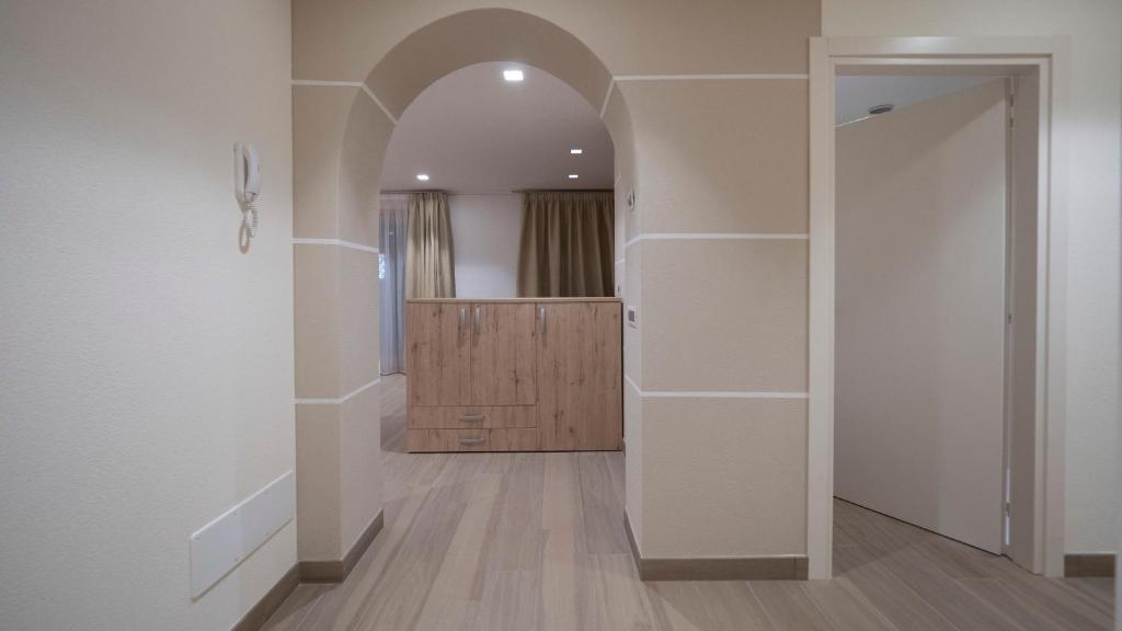 Mūsdienīgs interjers ar arhitektūras arku un koka mēbelēm, radot siltu un mājīgu atmosfēru. Gaismas tonis un tekstūra sniedz harmonisku noskaņu telpā.