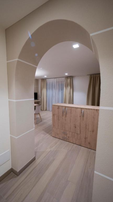 Mūsdienīga interjera skats caur arku uz viesistabu ar koka mēbelēm un dabiskiem toņiem.