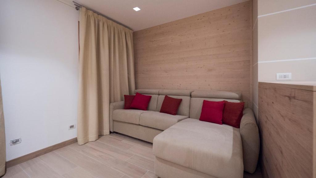 Mūsdienīga viesistaba ar gaišu dīvānu un sarkaniem spilveniem, koka apdare un aizkari rada mājīgu atmosfēru.