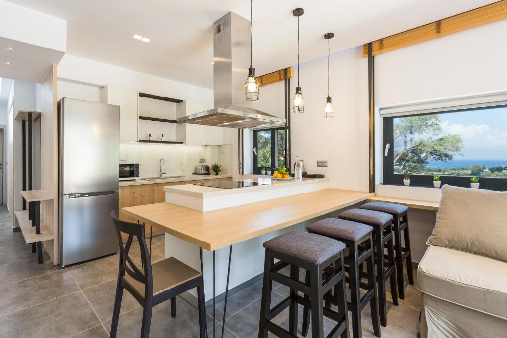 Mūsdienīga virtuve ar atvērtu plānojumu, koka darba virsmu un elegantiem gaismas ķermeņiem, kas rada siltu atmosfēru. Aiz loga redzams ainavīgs skats uz dabu.