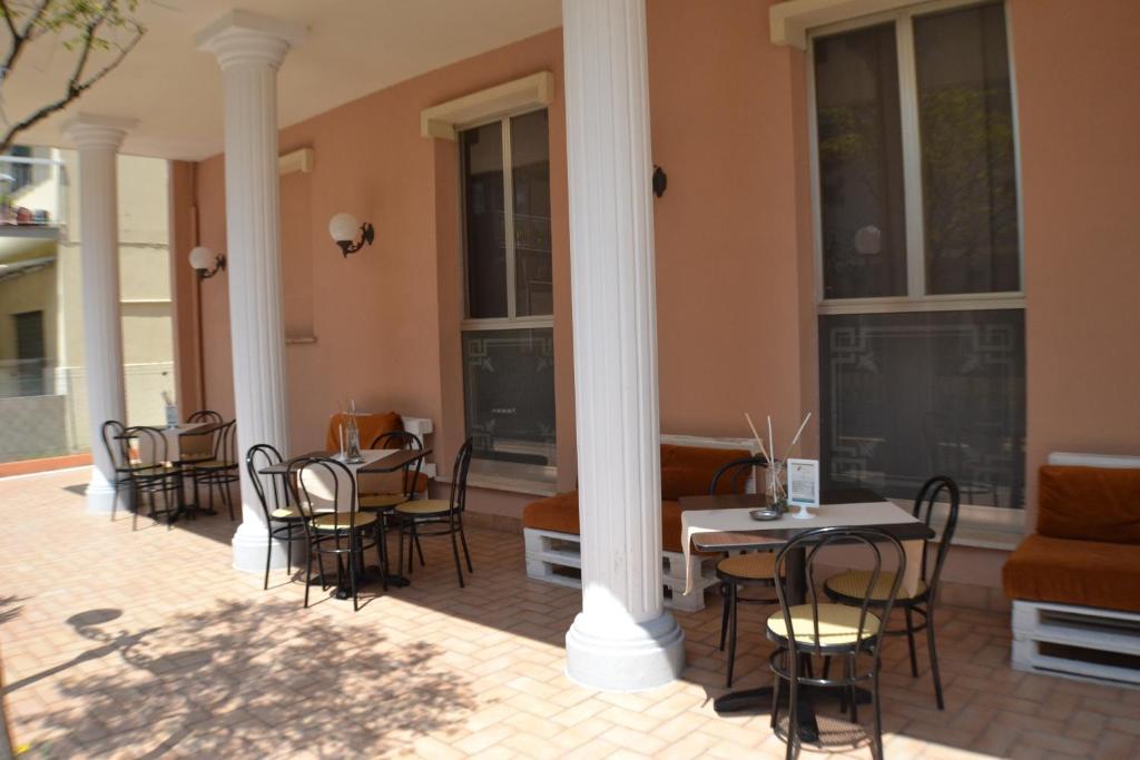 Āra kafejnīca ar melnu metāla mēbelēm un oranžiem dīvāniem, izvietota uz bruģēta celiņa, ar kolonnām un gaismas ķermeņiem pie sienas.