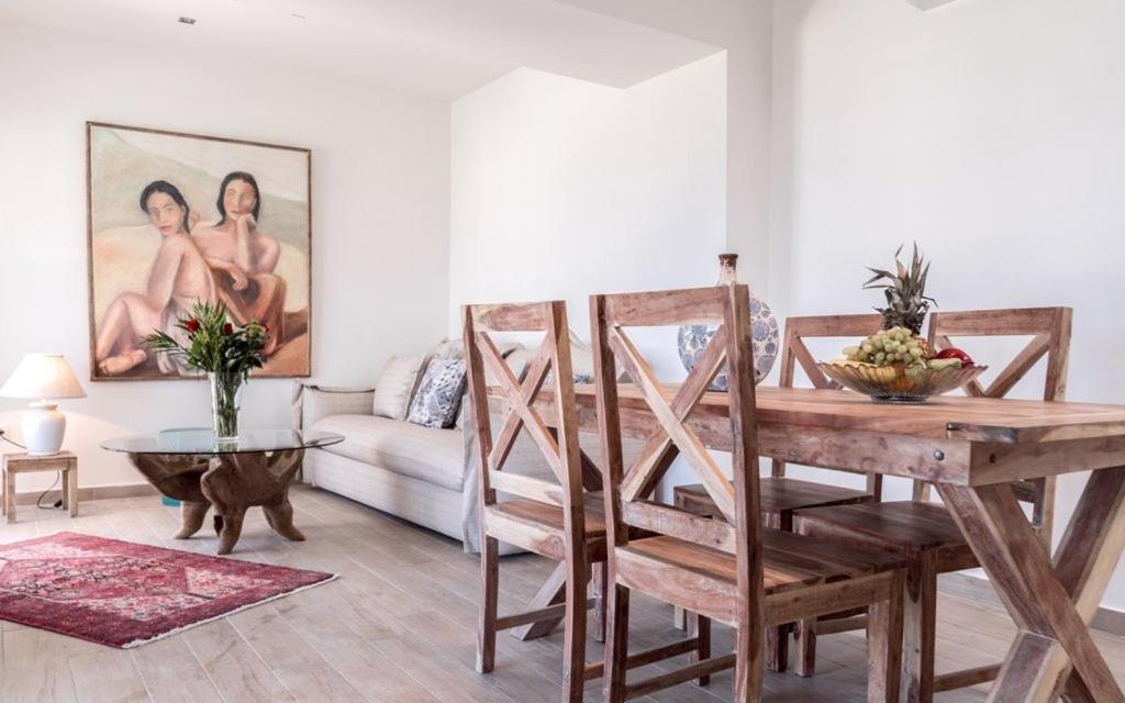 Mūsdienīgs dzīvojamās istabas interjers ar koka galdu un krēsliem, gleznainu mākslas darbu uz sienas un modernu dekoru. Atmosfēra ir silta un aicinoša, izceļot mājīgumu un stilu.