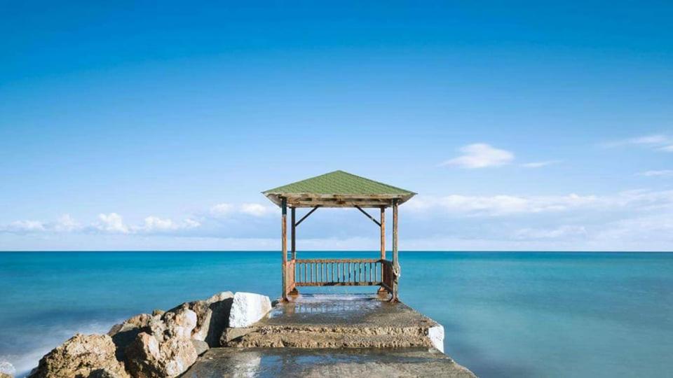 Koka paviljons uz mola pie mierīgas jūras ar skaidru zilu debesi. Ideāla vieta atpūtai un panorāmas baudīšanai.