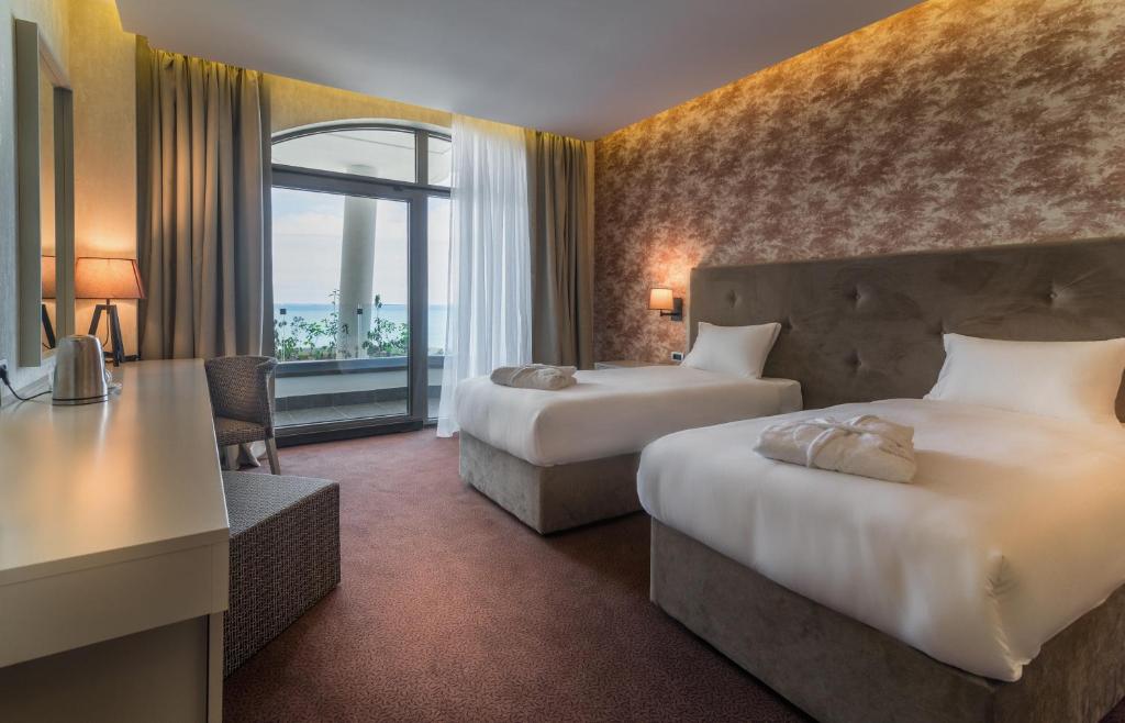 Mūsdienīgs viesnīcas numurs ar divām gultām, rakstāmgaldu un skaistu skatu uz jūru caur lieliem logiem. Interjers ir ērts un elegants, radot patīkamu atmosfēru.