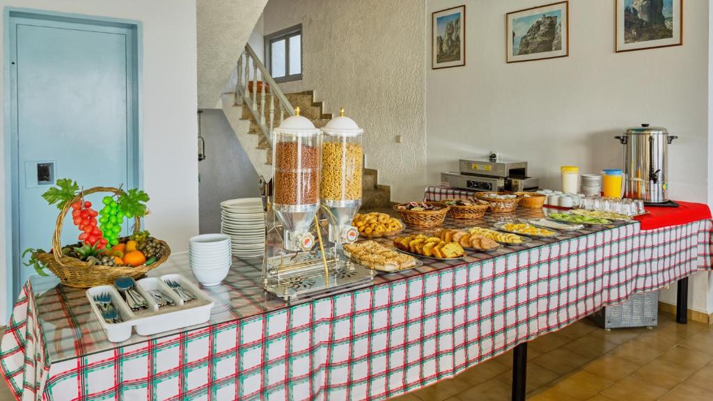 Brokastu bufete ar dažādiem ēdieniem, tostarp augļiem, cepumiem un graudaugiem, uz galda ar pārklājumu.