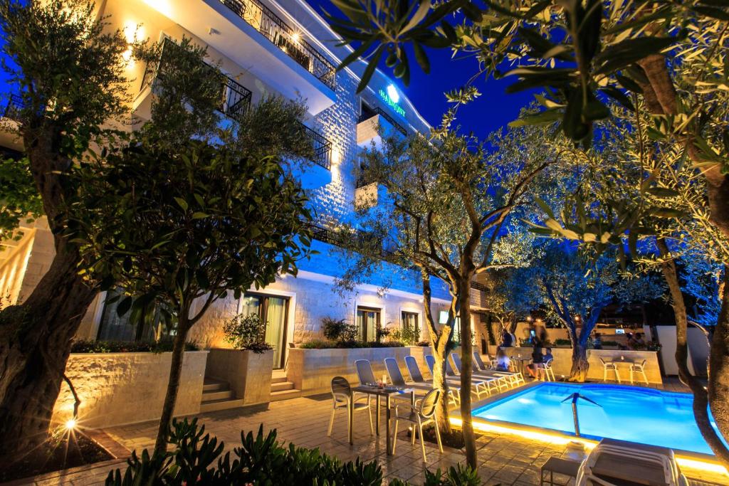 Elegants viesnīcas peldbaseins ar apgaismojumu nakts laikā, ko ieskauj koki un zaļumi, radot mierīgu atmosfēru. Ideāla vieta atpūtai un relaksācijai.