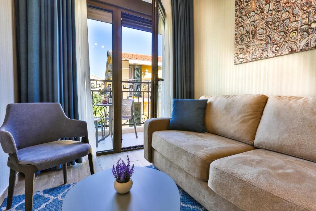 Mūsdienīga dzīvojamā istaba ar dīvānu, krēslu un galdu, kas rotāts ar ziediem. Lieli logi sniedz skatu uz āru un nodrošina dabīgu apgaismojumu.