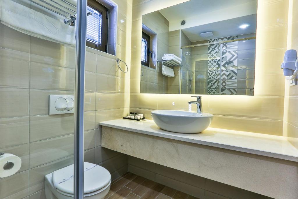 Mūsdienīgs vannas istabas interjers ar gaišām flīzēm, elegantu izlietni un dušu, kas rotāta ar ģeometrisku rakstu. Gaismas elementi rada patīkamu atmosfēru.