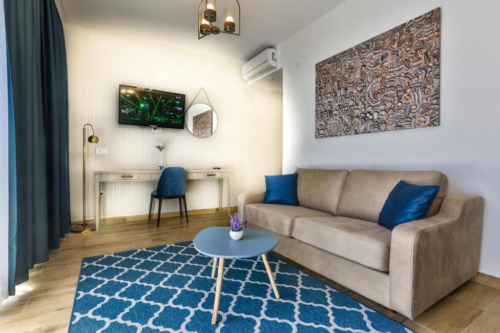 Mūsdienīgs viesistabas interjers ar dīvānu, mazu galdiņu un televizoru, kas piekārts pie sienas. Telpā ir dekoratīvs paklājs un mākslas darbs, radot siltu un aicinošu atmosfēru.