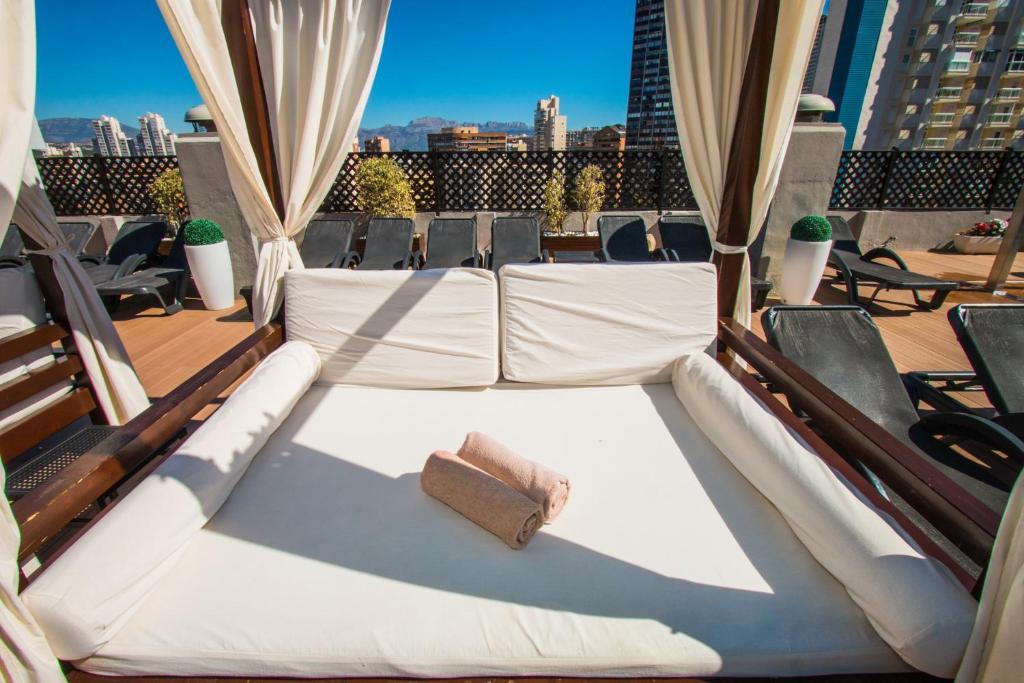 Grezns atpūtas stūrītis ar baltām spilveniem un dvieļiem, kas atrodas uz jumta terases, piedāvājot skatu uz pilsētu. Svaigs un saulains laiks veido ideālu atmosfēru relaksācijai.