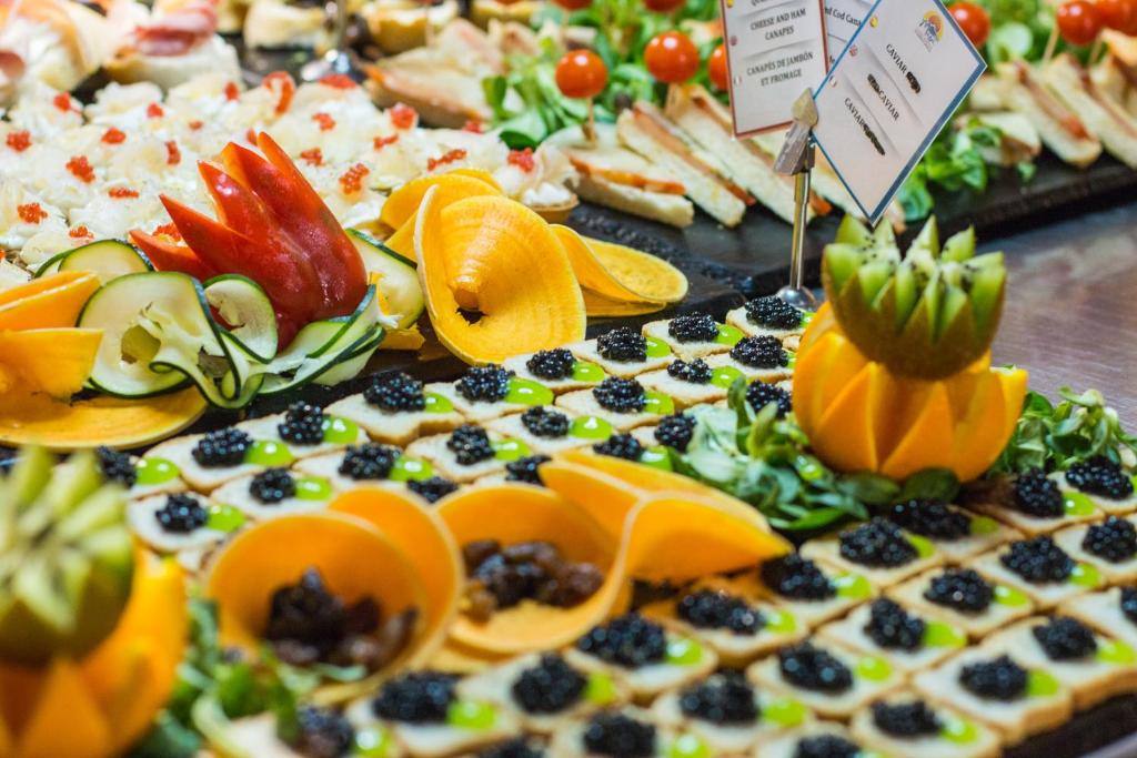 Krāsains uzkodu galdiņš ar dažādām delikatesēm, tostarp augļu un dārzeņu dekorācijām, kanapē un kaviāru. Šis vizuāli pievilcīgais ēdiens ir ideāli piemērots svinībām un pasākumiem.