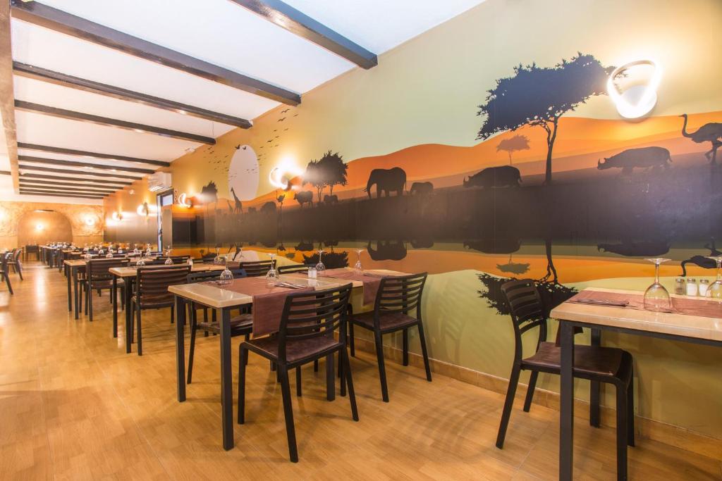 Restorāna iekšējā telpa ar galdiem un krēsliem, kas izvietoti garākā rindā, un uz sienas redzamu krāsainu gleznu ar afrikāņu dzīvniekiem un ainavām.