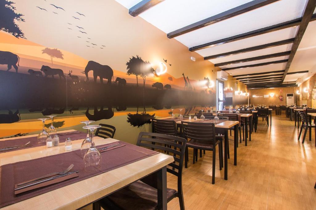 Restorāna interjers ar elegantām koka mēbelēm un krāšņu sienu gleznojumu, kas attēlo Āfrikas dzīvniekus saulrieta gaismā. Ideāla vieta relaksācijai un maltītēm.