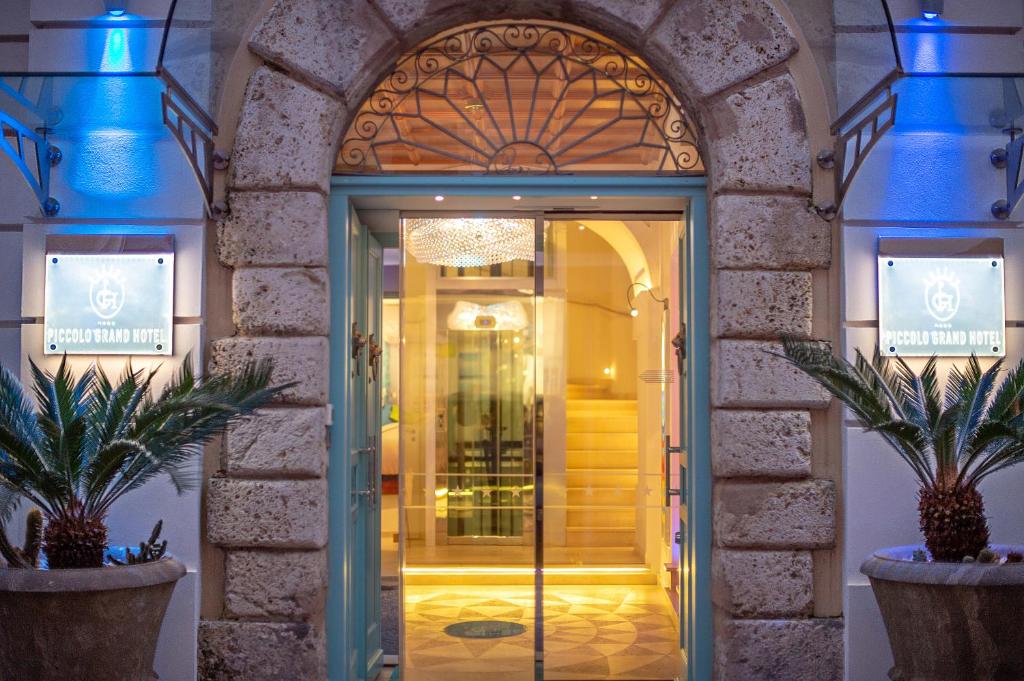Ieejas durvis uz Piccolo Grand Hotel ar modernu apgaismojumu un dekoratīviem augiem. Eleganta viesnīcas atmosfēra ar greznām detaļām.
