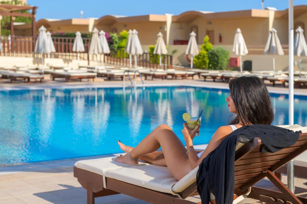 Sieviete, kas relaksējas pie Sun Beach Resort baseina ar kokteili rokā.
