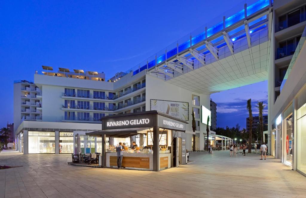Moderns tirdziņš ar gelato veikalu RIVAREN0, kas atrodas zem arhitektoniski interesantas struktūras, kas savieno ēkas. Nakts laikā, kad debesis ir tumšas, apkārt ir gaismas un cilvēki, kas pastaigājas.