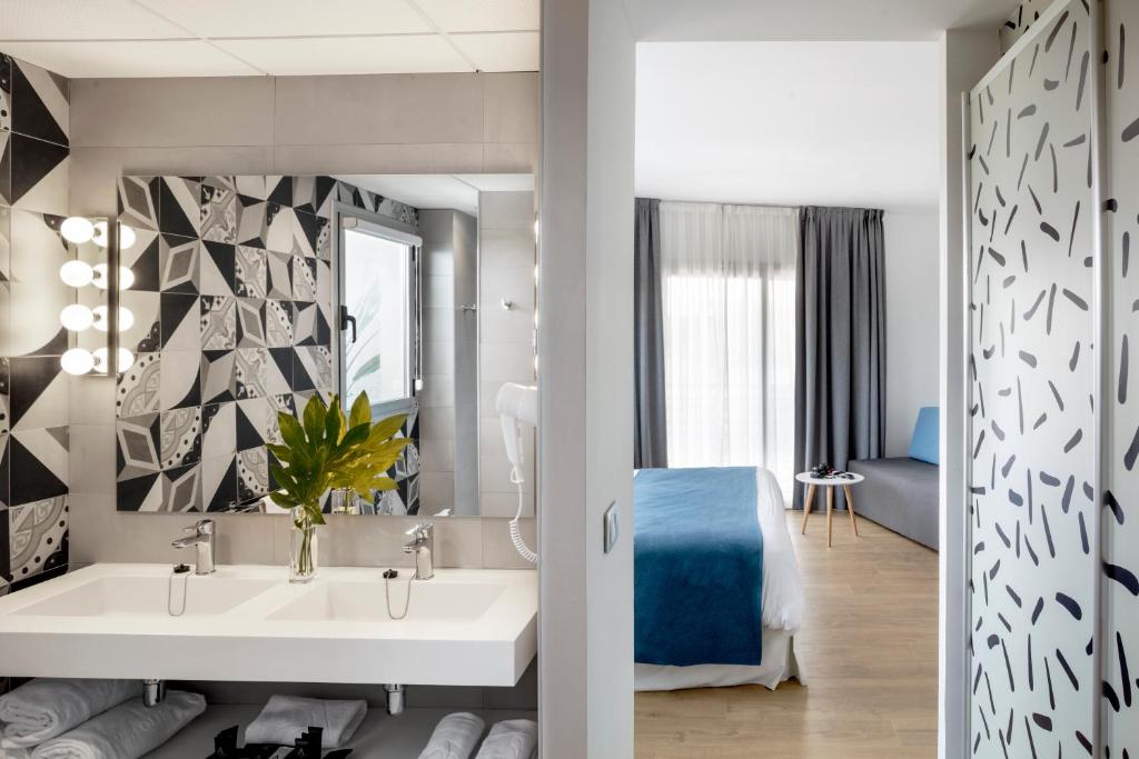 Mūsdienīgs vannas istabas un guļamistabas interjers ar melnbaltu flīžu dizainu un dabīgu zaļumu. Telpa ir gaiša un ērta, ar liela loga gaismu un komfortablu mēbeļu izkārtojumu.