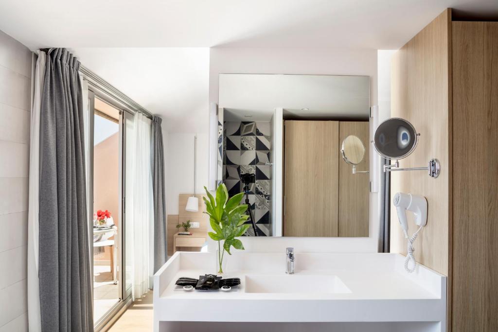 Moderns vannas istabas interjers ar gaišu krāsu paleti, plašu spoguli un augu dekoru. Logi ar aizkariem nodrošina dabisko apgaismojumu un piekļuvi terasei.