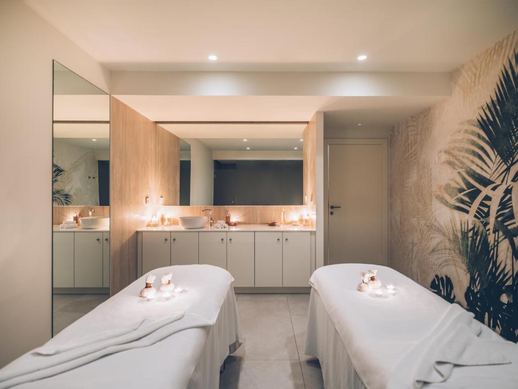Mūsdienīgs spa telpa ar divām masāžas gultām, siltu apgaismojumu un relaksējošu atmosfēru. Sienas rotā augu motīvi, radot mierīgu un harmonisku vidi.