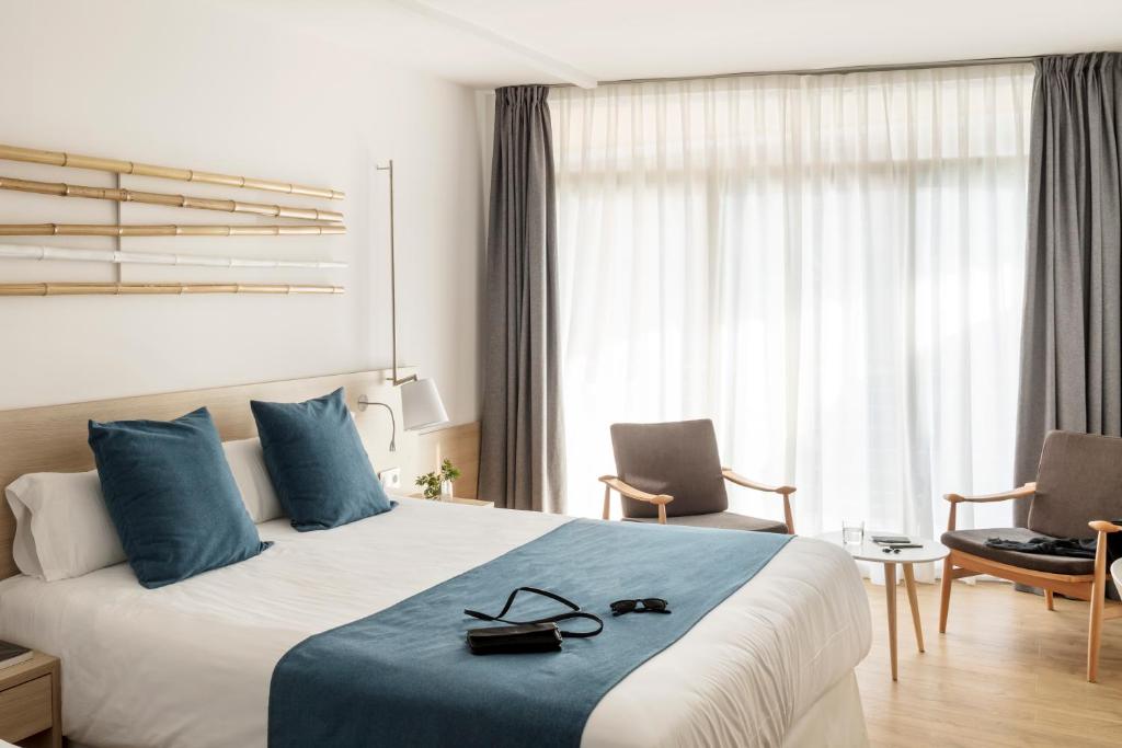 Moderns viesnīcas numurs ar gultu, dekoratīvām spilveniem un ērtām krēslām. Labi apgaismots ar logiem, kas ļauj ienākt dabiskajai gaismai.