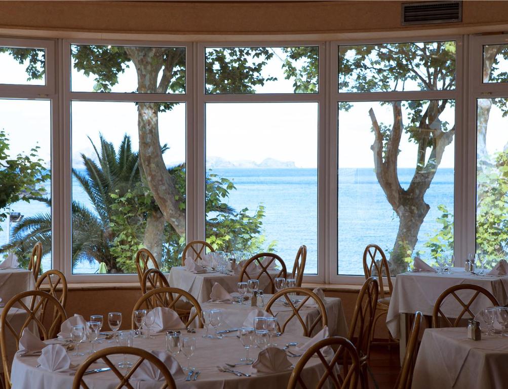 Elegant restaurant interior with tables set for dining, featuring large windows that offer a scenic view of the sea and surrounding trees.
