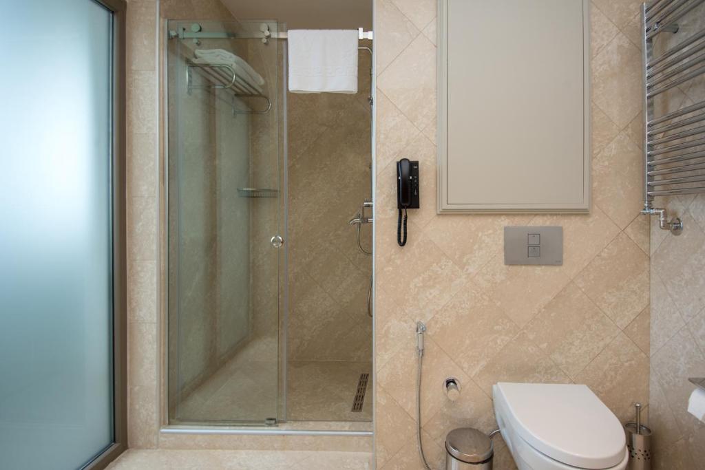 Mūsdienīgs vannas istabas interjers ar dušas kabīni, tualeti un vannas dvieļu turētāju. Telpa ir izklāta ar gaišām flīzēm, radot elegantu un tīru atmosfēru.