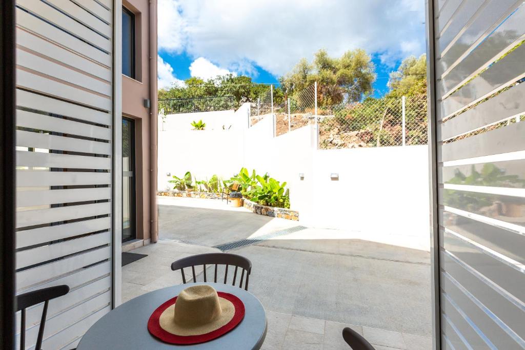 Skats no loga uz saulainu āra terasi, kurā redzams galds ar cepuri un dārza augi. Svaiga un mierīga atmosfēra.