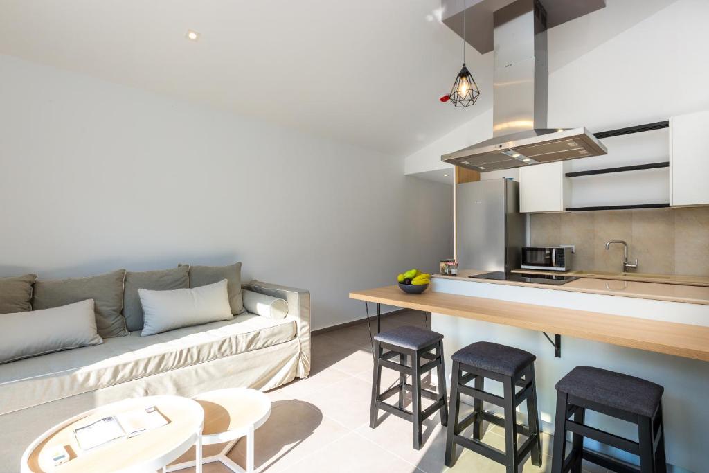 Mūsdienīga virtuve ar atvērtu plānojumu, kurā redzams dīvāns un bāra krēsli pie virtuves letes. Gaisma plūst cauri telpai, radot siltu un viesmīlīgu atmosfēru.