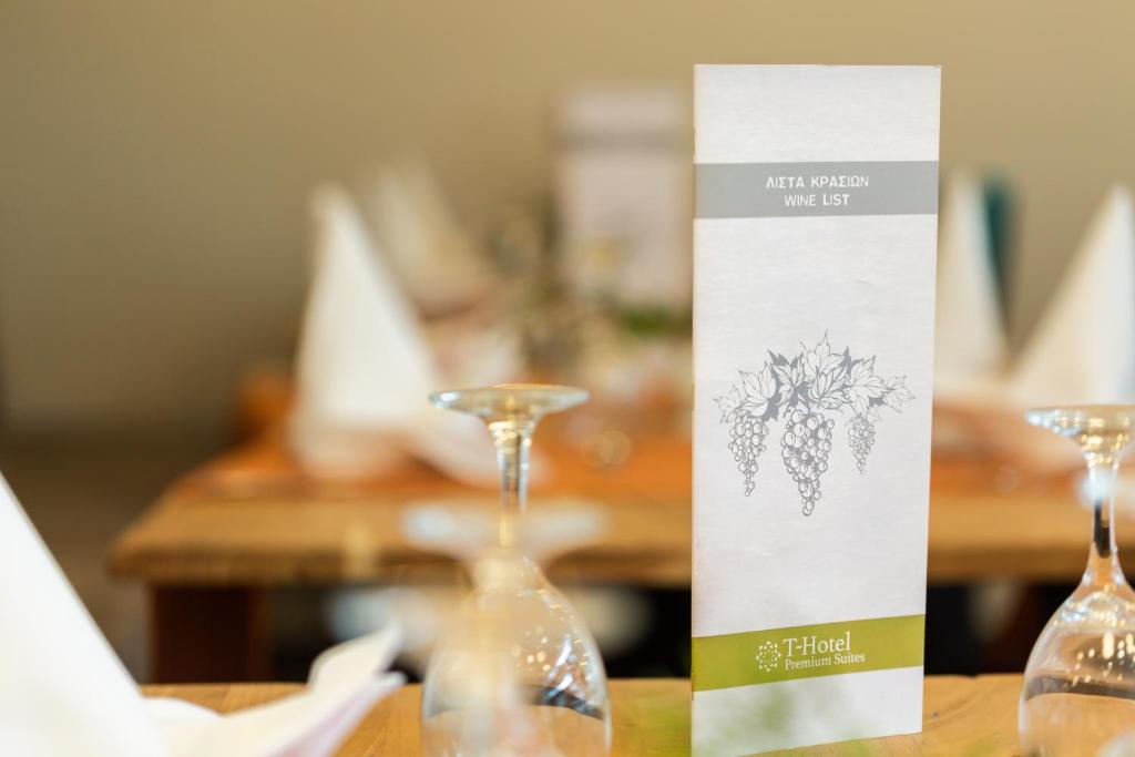 Vīna saraksta stends ar vīnogu ilustrāciju un T-Hotel Premium Suites logotipu, novietots uz galda.