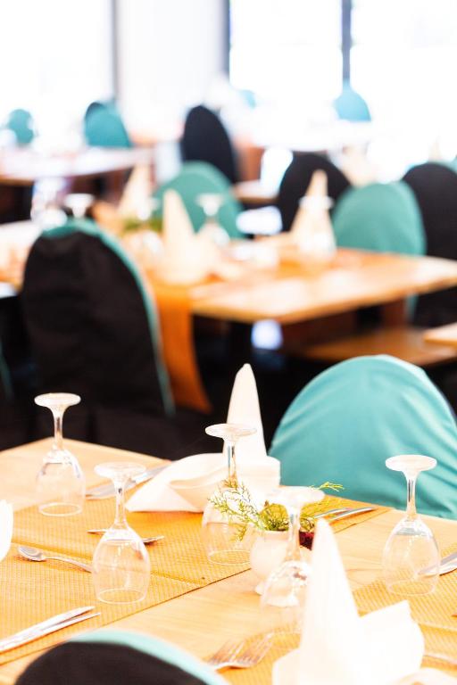 Elegantā restorāna interjers ar galdiem, kas klāti ar zilu un melnu tekstilizstrādājumu, ar glāzēm, galda piederumiem un dekoratīviem elementiem.