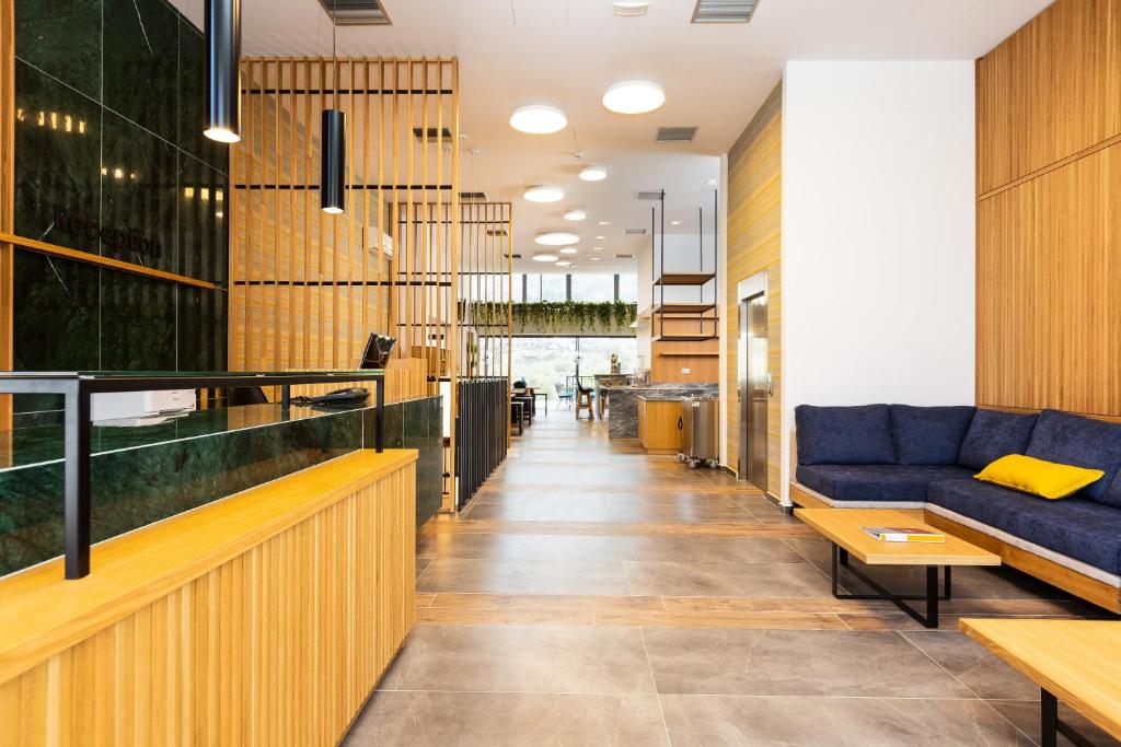 Mūsdienīga viesnīcas recepcija ar koka un zaļā akmens akcentiem, plašs interjers un ērtas sēdvietas. Gaismas un augi rada patīkamu atmosfēru.