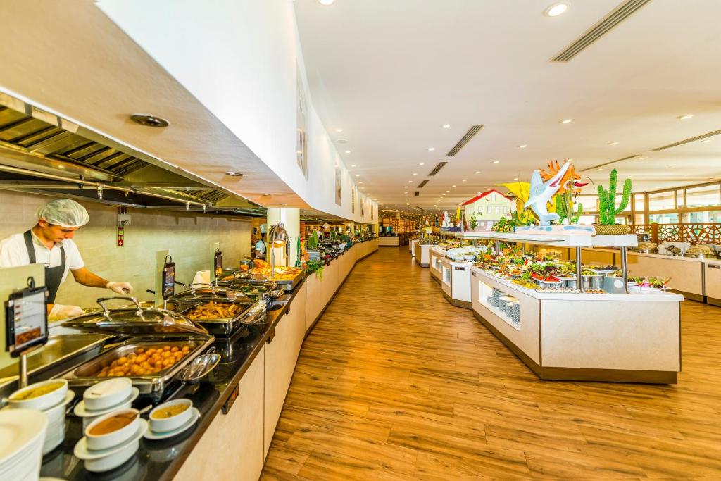 Lielisks restorāna bufetes skats ar dažādiem ēdieniem un apkalpojošo personālu, kas gatavo ēdienus. Gaismas un moderns interjers veido viesmīlīgu atmosfēru.