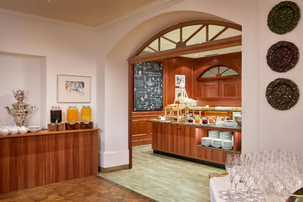 Eleganta restorāna iekārtojums ar bufetes galdu, kas piedāvā dažādus dzērienus un ēdienus. Sienā redzams melnbalts krāsojums un dekoratīvi šķīvji.