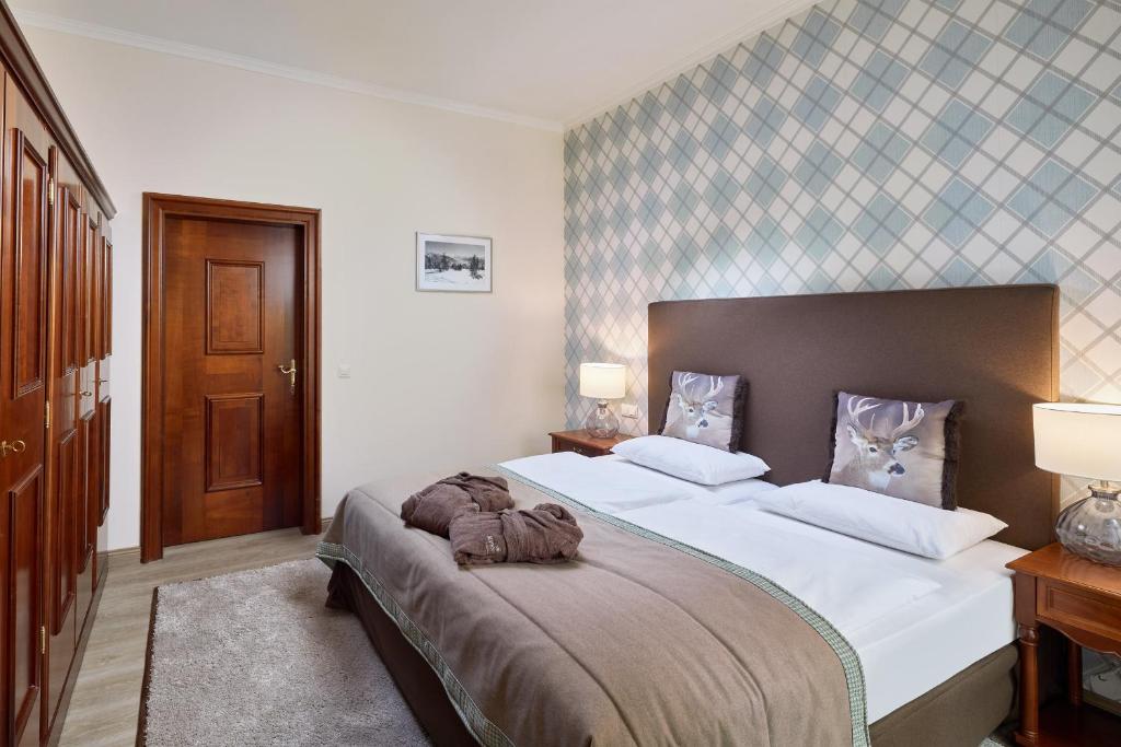 Mūsdienīgs guļamistabas interjers ar divguļamo gultu, dekoratīvām spilvenēm un koka skapjiem. Sienas ir noformētas ar modernu ģeometrisku rakstu.