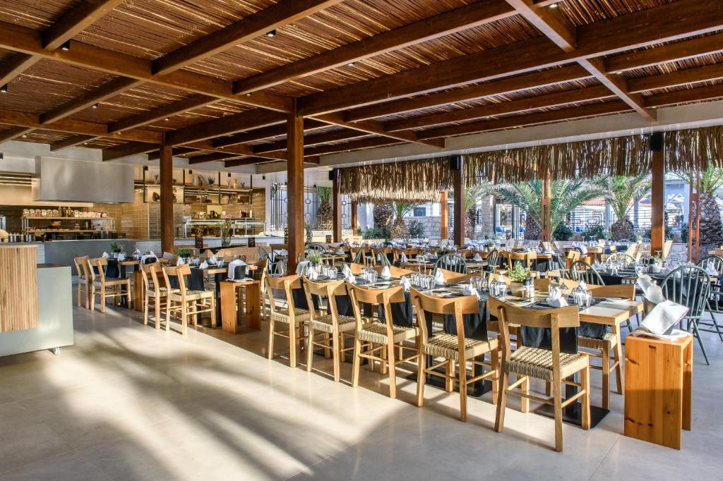 Mūsdienīgs restorāna interjers ar koka konstrukcijām, plašu galdu izvietojumu un skatu uz palmu dārzu. Gaisma un dabiskie materiāli rada mājīgu atmosfēru.