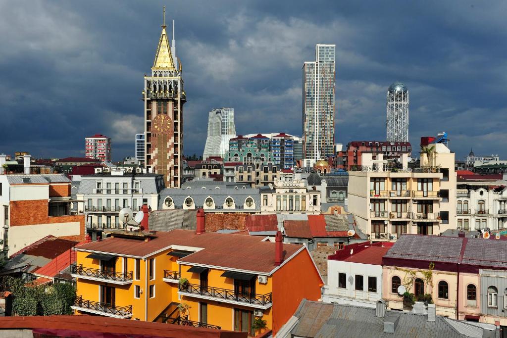Pilsētas skats ar daudzveidīgu arhitektūru, kur redzami vēsturiskie un modernie ēkās, kā arī debesis, kas ir apmākušās.