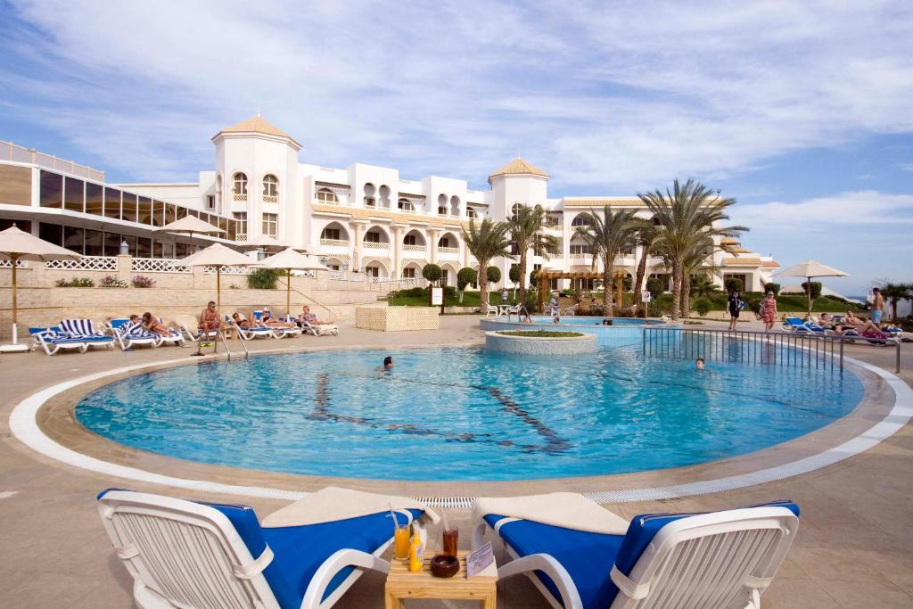 Baseins pie Old Palace Resort Sahl Hasheesh ar palmām un sauļošanās krēsliem.