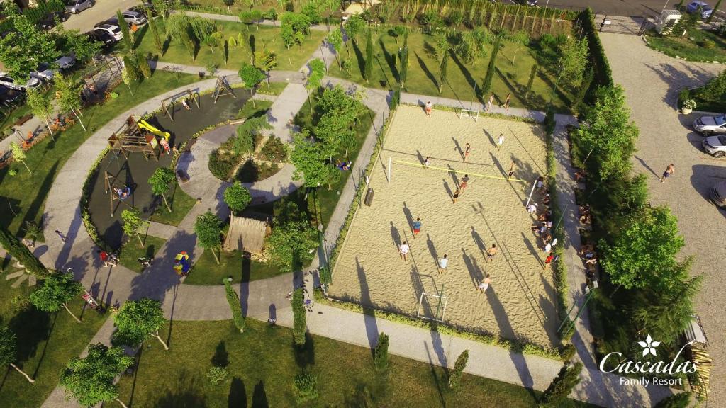 Bērnu spēļu laukums un pludmales volejbola laukums, kas atrodas "Cascadas Family Resort". Ainava ir zaļa un plaša, ar bērniem, kas spēlējas un sporto.