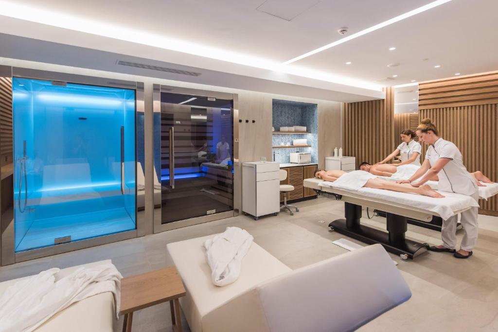 Mūsdienīga spa telpa ar masāžām un relaksācijas zonām, kur profesionālas masieres sniedz pakalpojumus. Telpā redzami moderna dizaina elementi un gaišas krāsas.