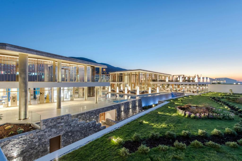 Mūsdienīgs arhitektūras komplekss ar stikla fasādēm un apzaļumotu teritoriju, kas izgaismota saulrieta gaismā. Svaigs un stilīgs dizains, kas piedāvā elegantu atmosfēru.