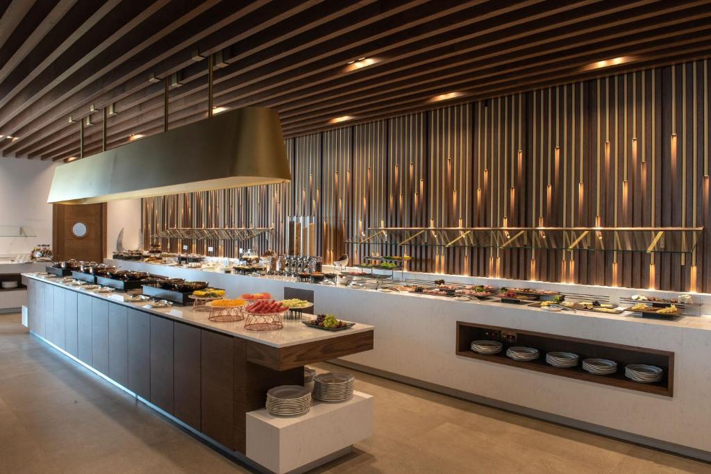 Mūsdienīga bufetes zona ar elegantu dizainu, kurā redzams plašs ēdienu klāsts un stilīgi apgaismojumi. Ideāli piemērota restorāniem vai viesnīcām.