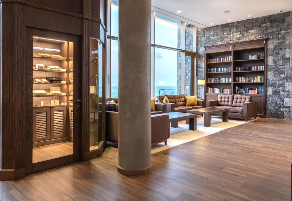 Mūsdienīga bibliotēka ar plašām logiem un ērtiem dīvāniem, kurā ir grāmatu plaukti un izsmalcināti interjera elementi. Telpā ir arī stikla skapītis ar dažādām kolekcijām.