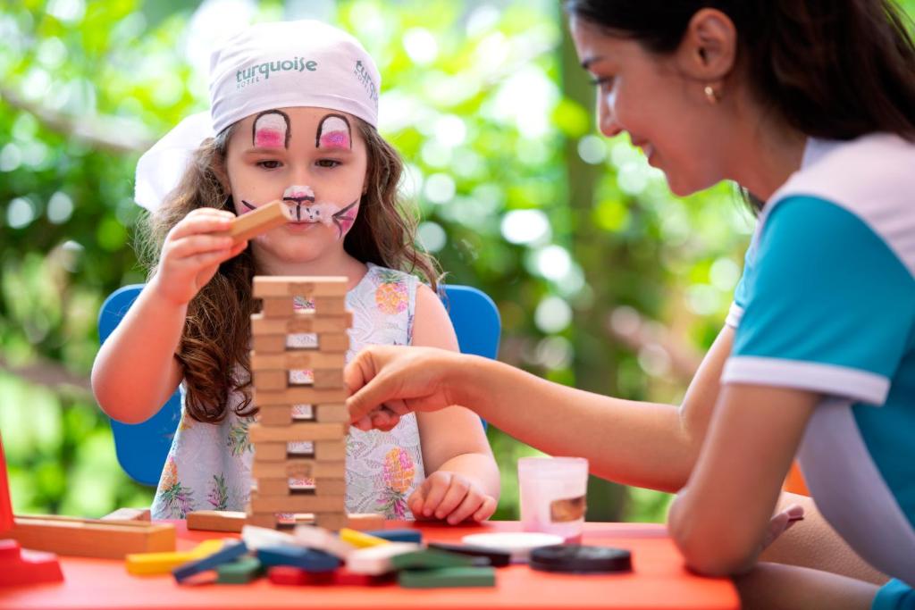 Bērns spēlējas ar koka spēli Turquoise Hotel, kamēr pieaugušais palīdz.