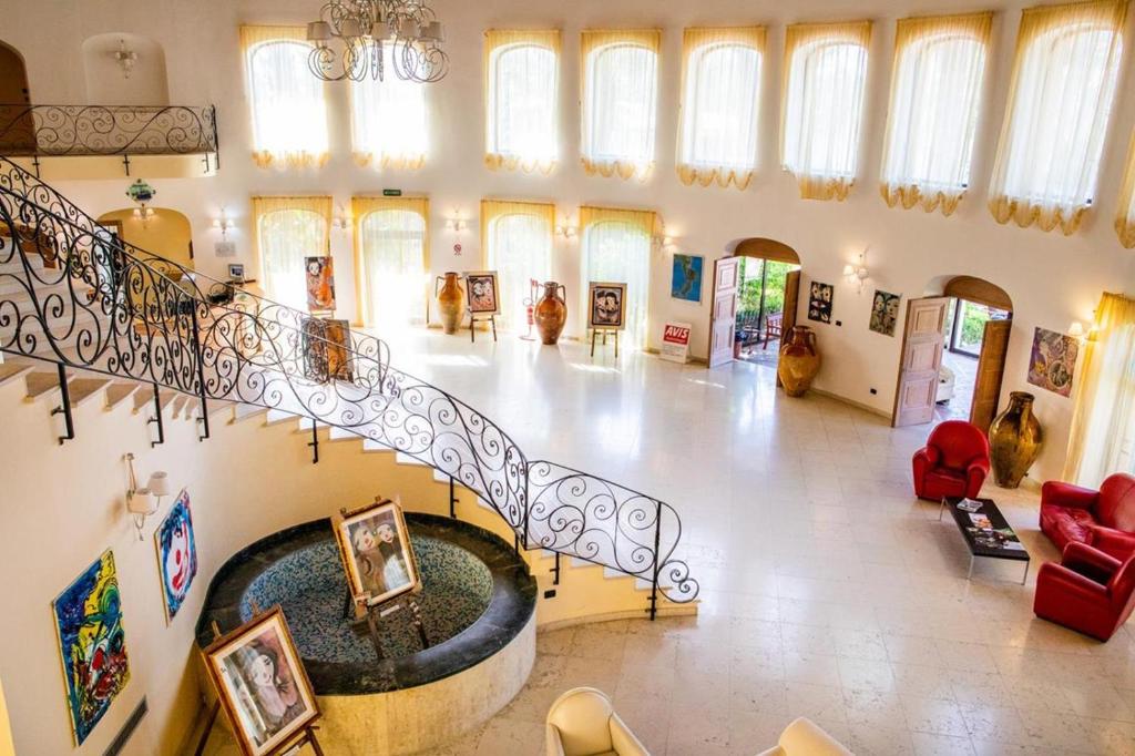 Plaša, eleganta telpa ar spirālveida kāpnēm, mākslas darbiem un gaisīgu apgaismojumu, kas rada viesmīlīgu atmosfēru. Redzamas sarkanās krēslu grupas un dekoratīvas vāzes.