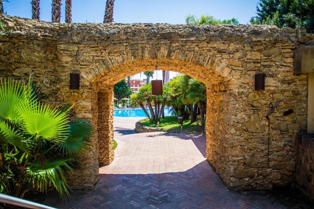 Akmens arka, caur kuru redzams baseins un zaļumi, rada relaksējošu un viesmīlīgu atmosfēru. Šis ainavas elements ir ideāls, lai uzsvērtu atpūtas vietas burvību.