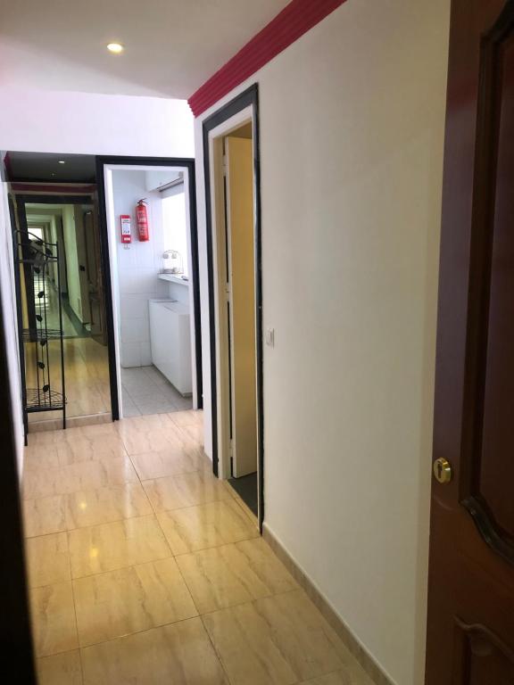 Gaišs un plašs koridors ar flīžu grīdu, kurā redzamas vairākas durvis un izeja uz virtuvi. Koridora sienas ir baltas, ar sarkanu apmalīti augšā.