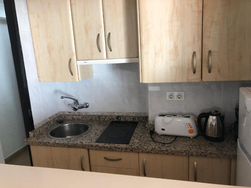Kompaktā virtuve ar koka skapīšiem, granīta virsmu un nepieciešamajiem sadzīves tehnikas elementiem, tostarp elektrisko tējkannu un tosteri.
