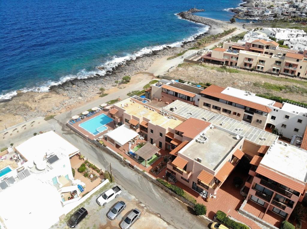 Skats uz piekrasti ar viesnīcu kompleksu, baseinu un akmeņainu pludmali. Zilais jūras ūdens un saulainā debesis veido relaksējošu atmosfēru.